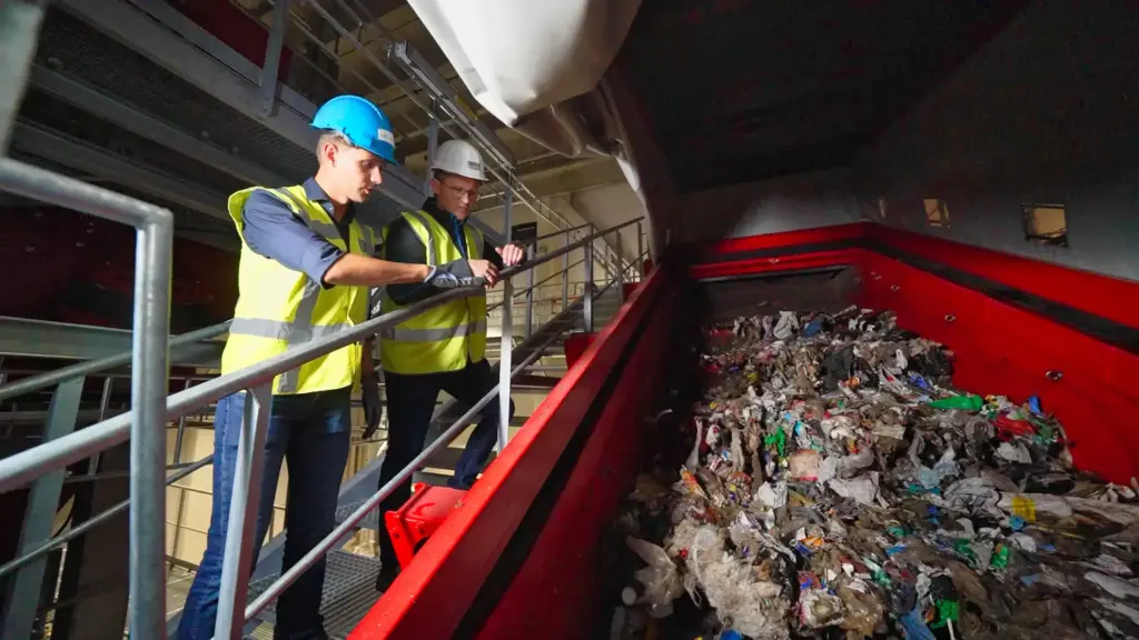 Zwei Recyclingexperten blicken auf eine SPALECK Siebmaschine in einer großen Recyclinganlage für Hausmüll.