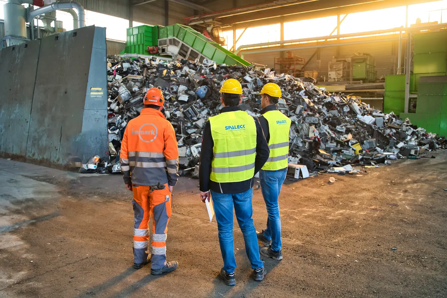Immark Projektleiter und zwei Siebmaschinenexperten von SPALECK stehen vor dem unzerkleinerten Inputmaterial für die neue Elektroschrottaufbereitungsanlage